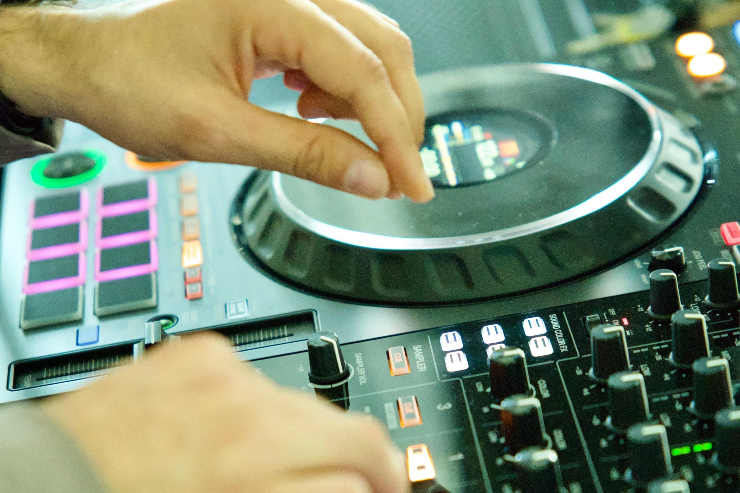Nahaufnahme: Hände regeln Fader und Jog-Wheel eines DJ-Controllers