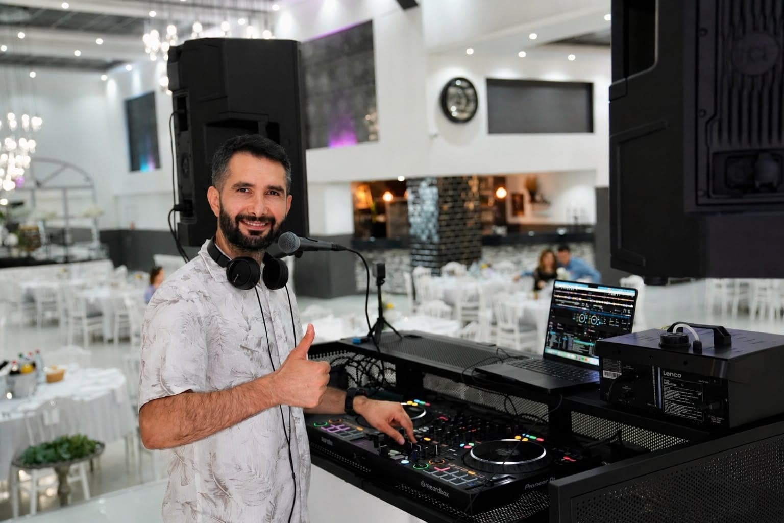 Veysel Durmuş am DJ-Pult im Festsaal, lächelnd in die Kamera