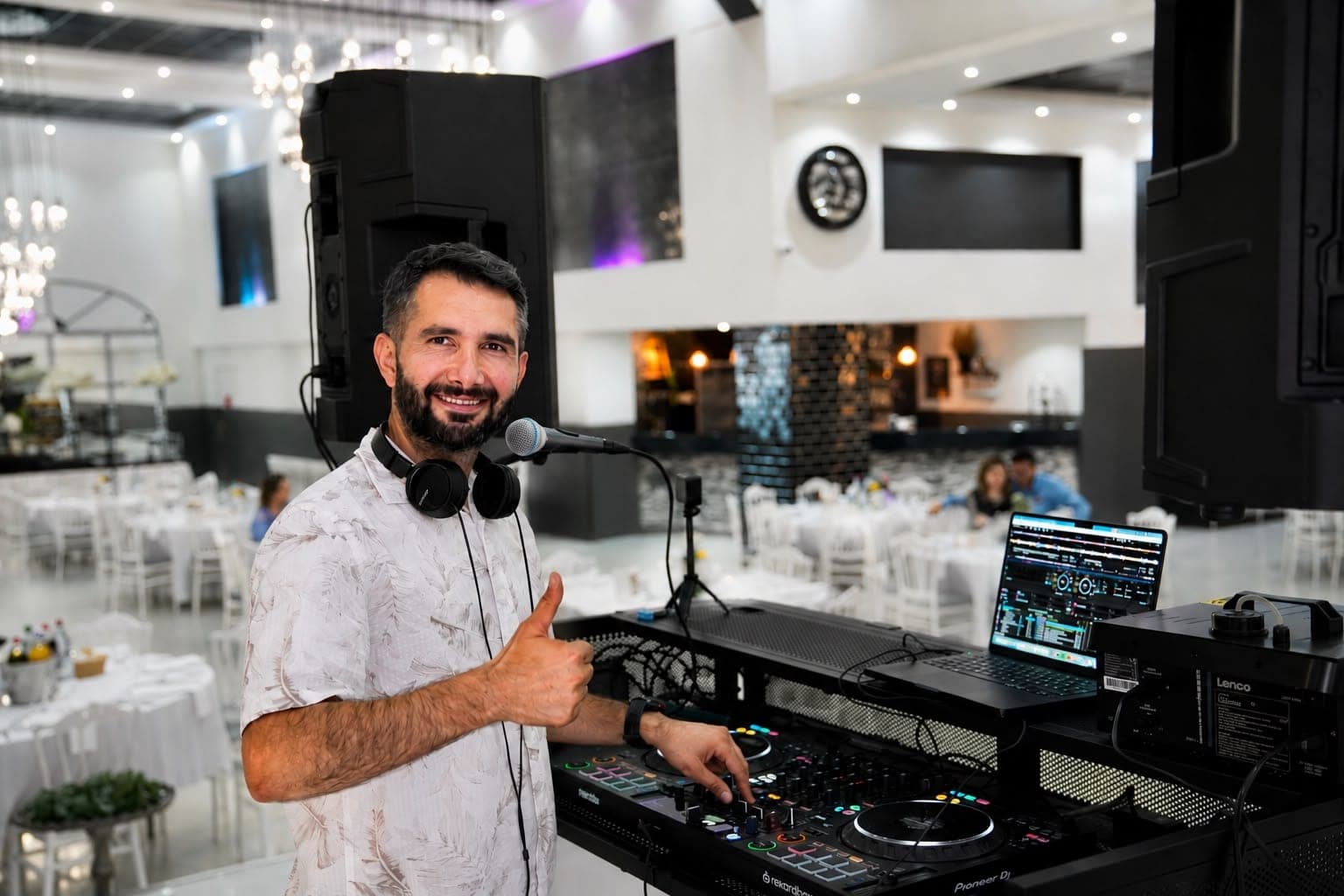Veysel Durmuş am DJ-Pult in einem großen Festsaal mit Kronleuchtern und eingedeckten Tischen
